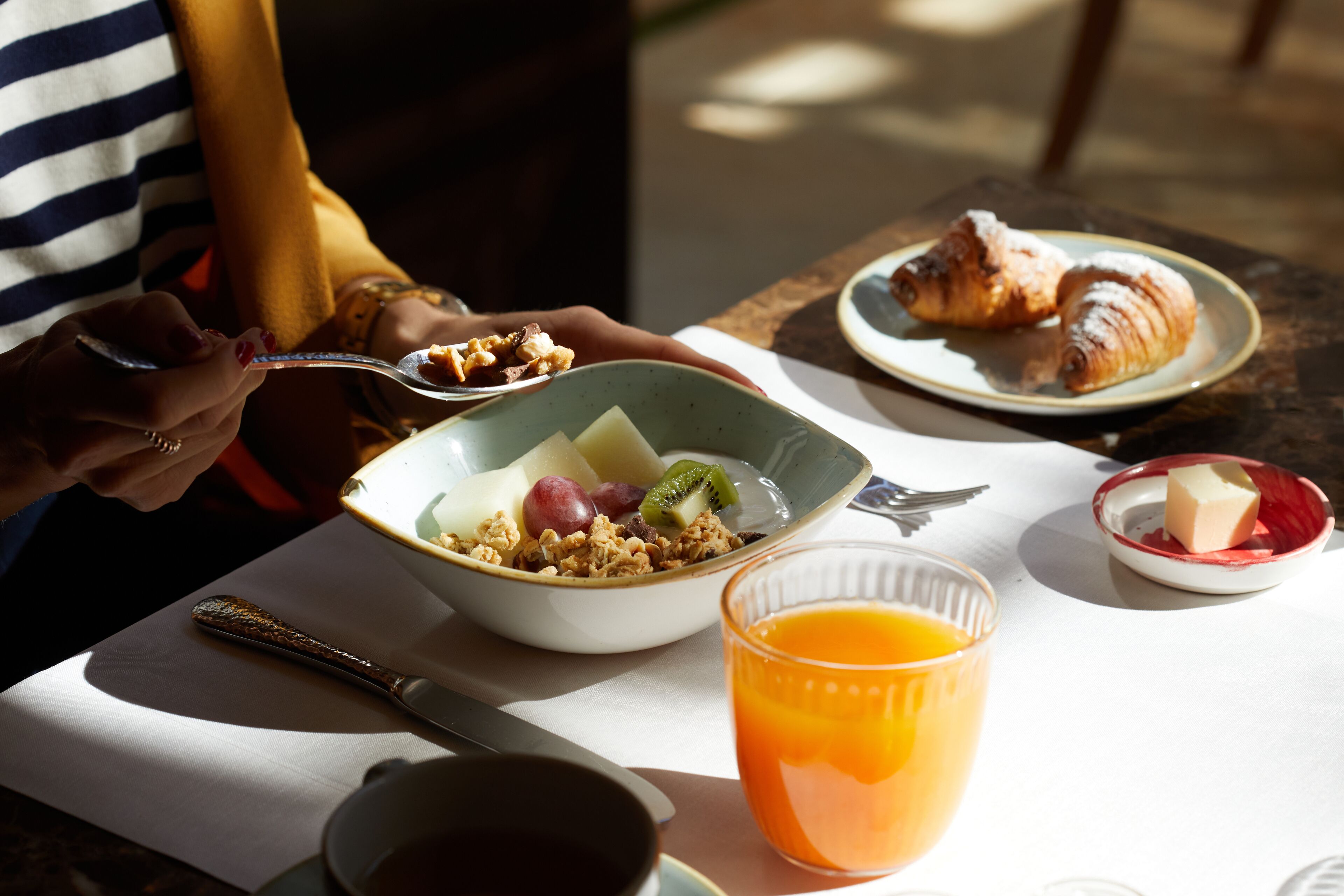 A breakfast setting with a bowl of cereal, fruits, and a glass of orange juice on a table.