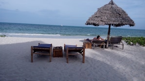 A beach with wooden lounge chairs and a thatched umbrella. - Blue Earth Beach Bungalows (Jambiani)
