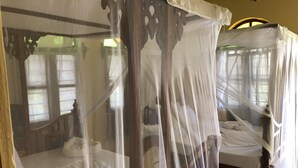 A room with a bed covered by a mosquito net, a wooden headboard, and a patterned floor. - Blue Earth Beach Bungalows (Jambiani)