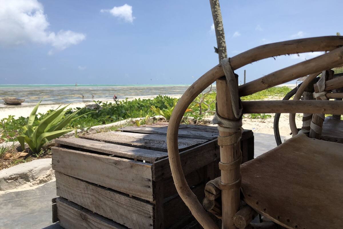 Un carro de madera con una rueda, una pila de cajas de madera, y vistas a la playa y al océano.