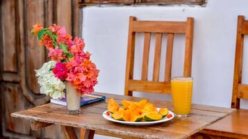 A wooden table with a plate of sliced fruit, a glass of orange juice, and a vase of flowers.