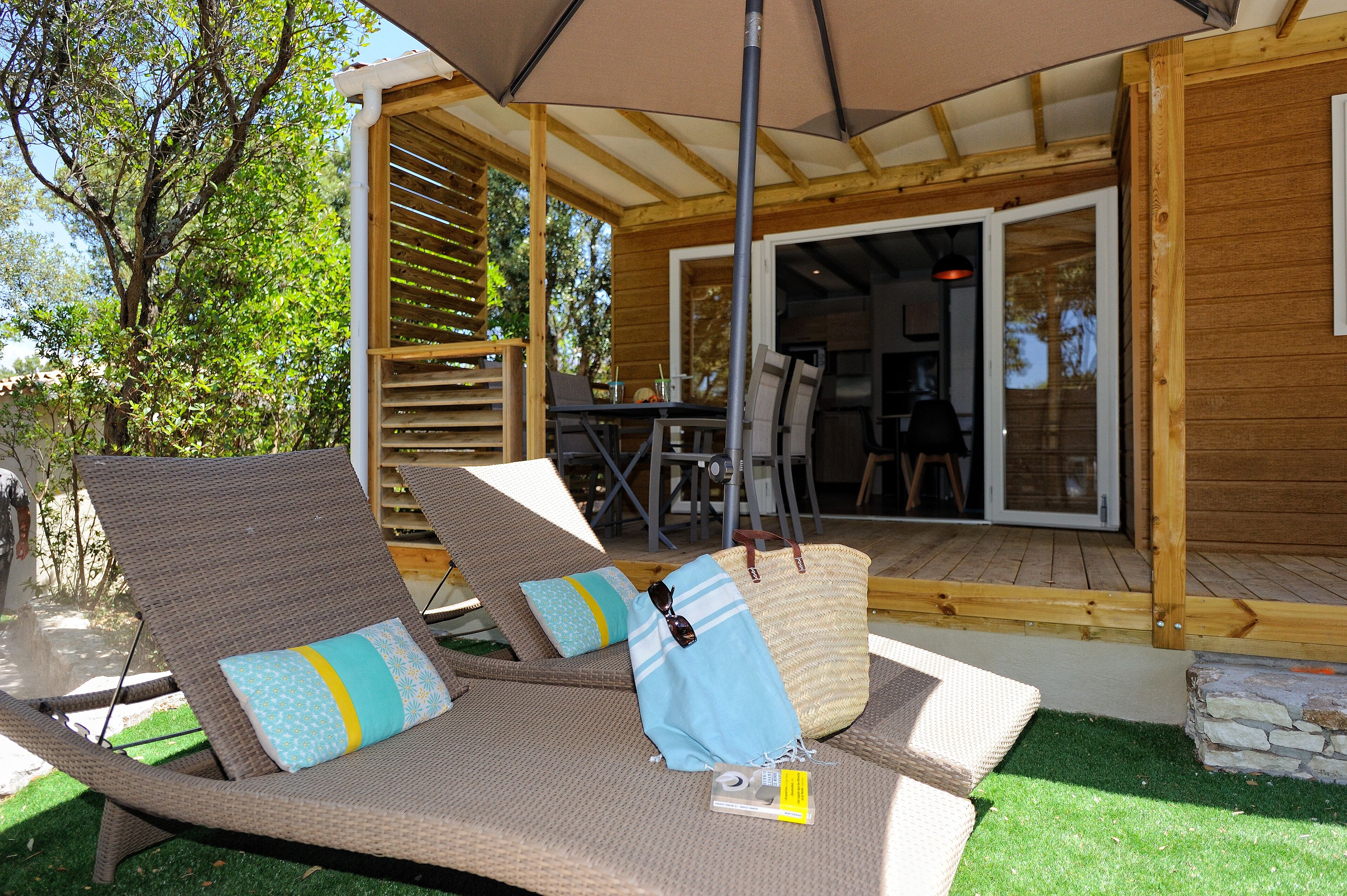 A covered outdoor seating area with wicker lounge chairs, a table, and a large umbrella.