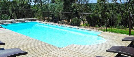 A swimming pool with a wooden deck and lounge chairs.