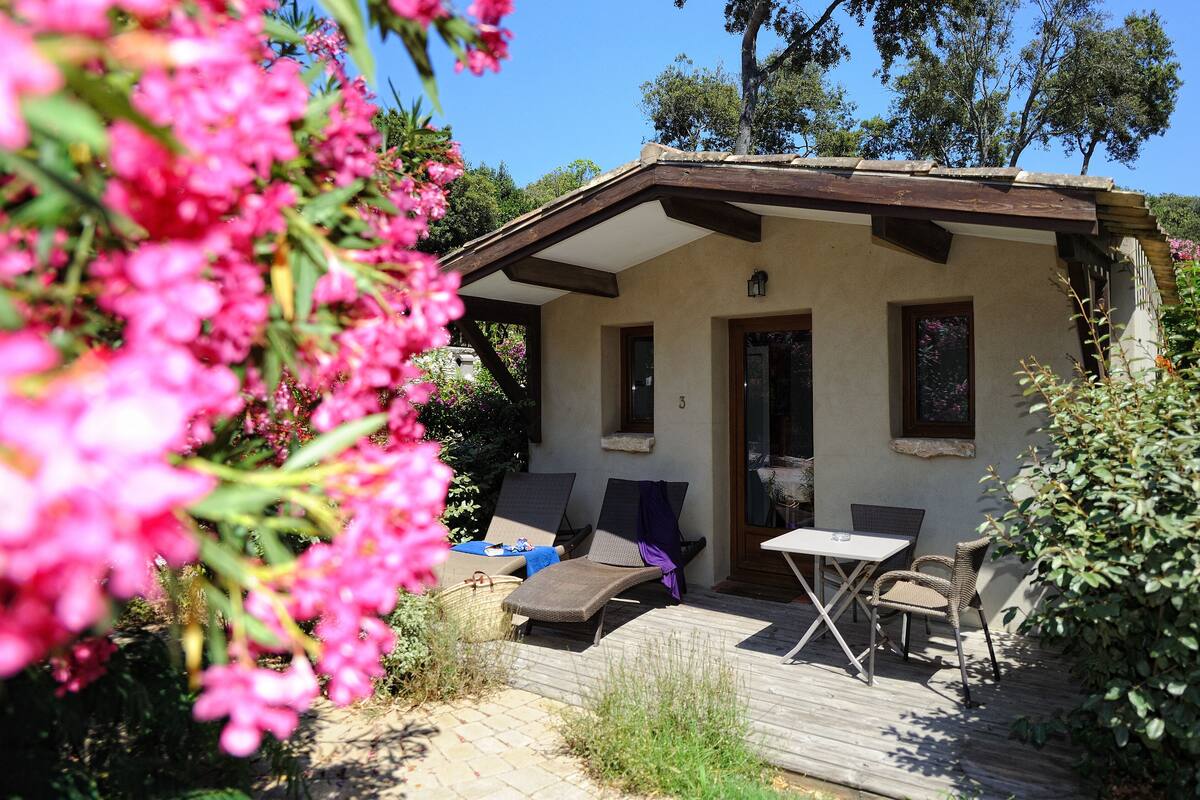 Una casita con una terraza de madera, dos sillones, una mesa y una silla.
