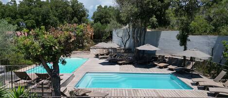 Una piscina rectangular con una terraza de madera y sillas reclinables.