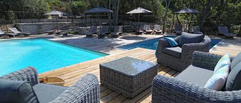A poolside area with wicker furniture, umbrellas, and a wooden deck.