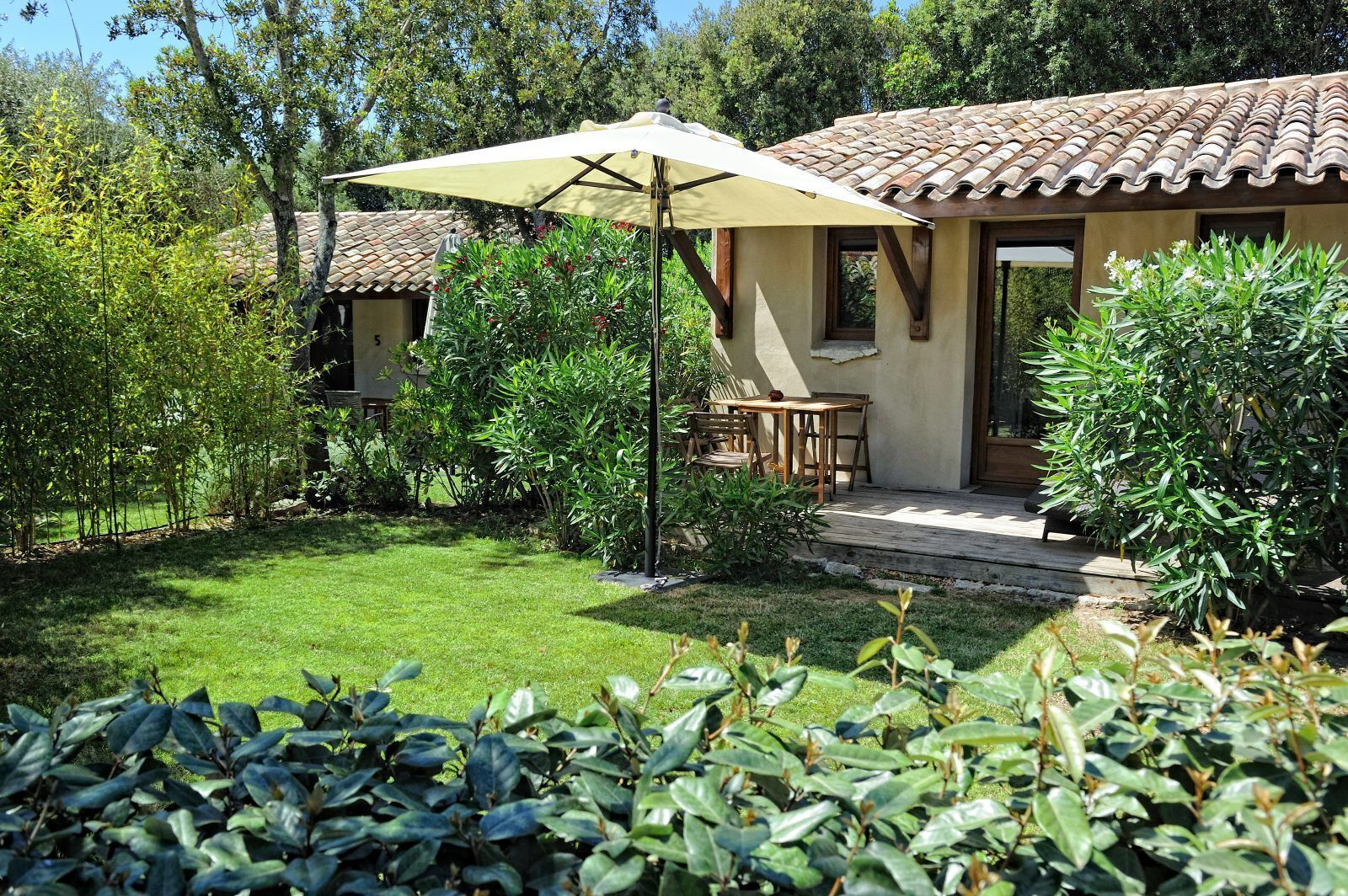 Patio con tavolo e sedie, immerso nel verde e affiancato da un edificio con tetto in tegole.