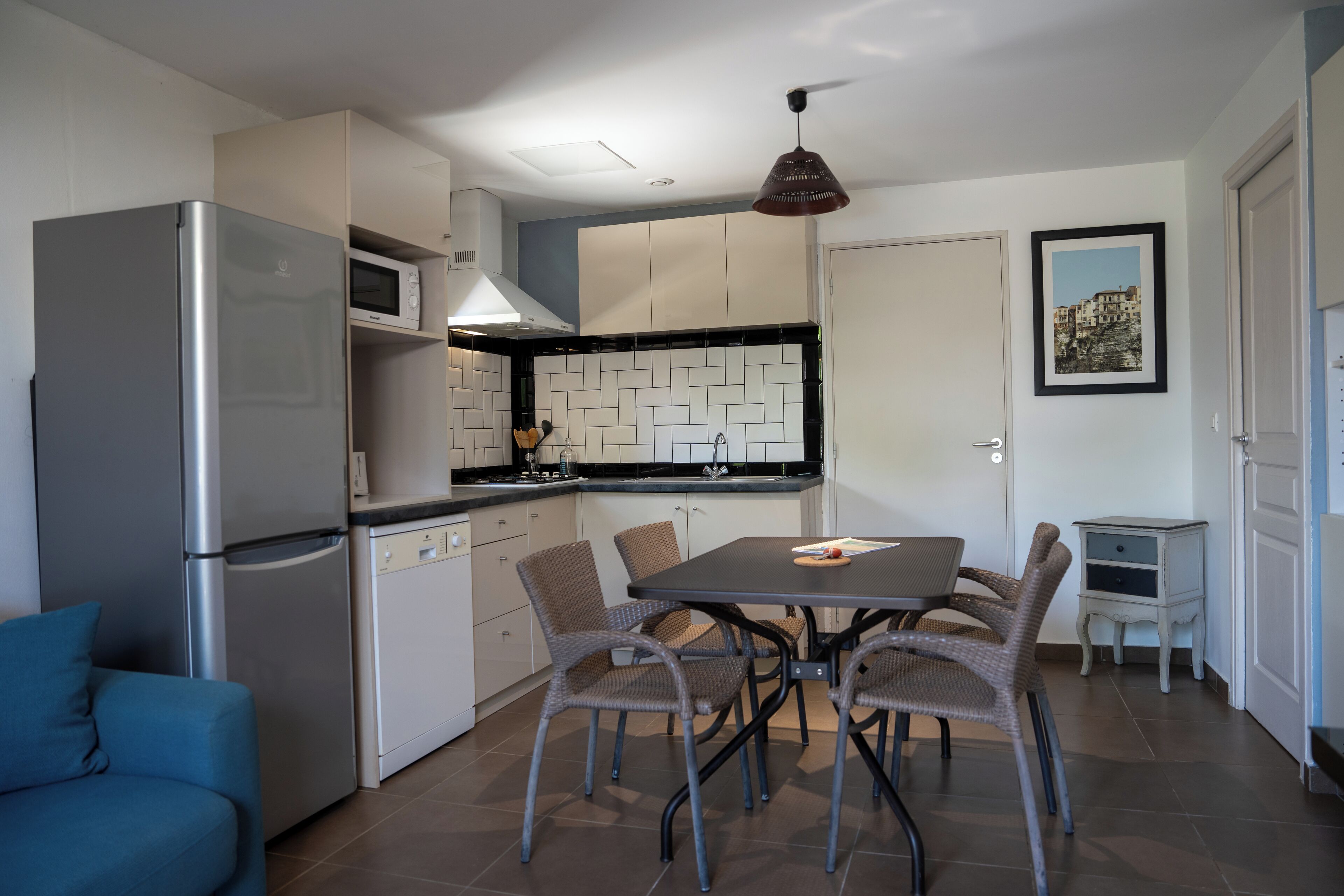 A compact kitchen with a dining table, chairs, a refrigerator, microwave, and a small cabinet.