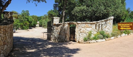 A stone entrance gate to a property named 'Résidence Sophia' with a dirt path leading to it, surrounded by trees and greenery.