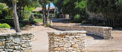 Un sendero de piedra que conduce a un edificio rústico con techo de tejas, rodeado de abundante vegetación y muros de piedra.