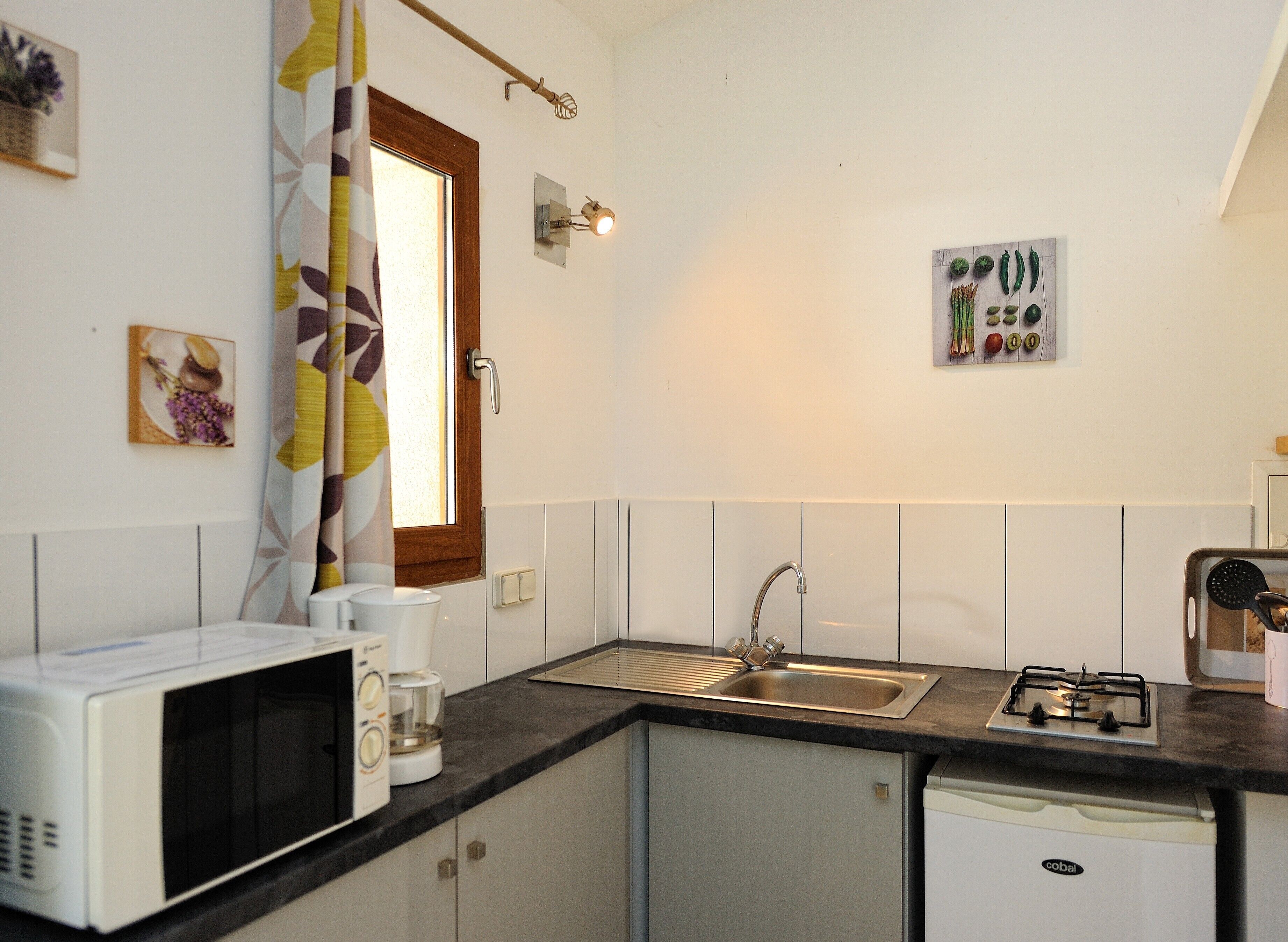 A compact kitchen with a microwave, coffee maker, sink, and a gas stove.