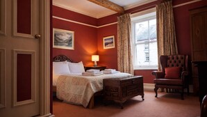 A room with a bed, a chair, a lamp, and a window with curtains. - Wynnstay Hotel (Machynlleth)