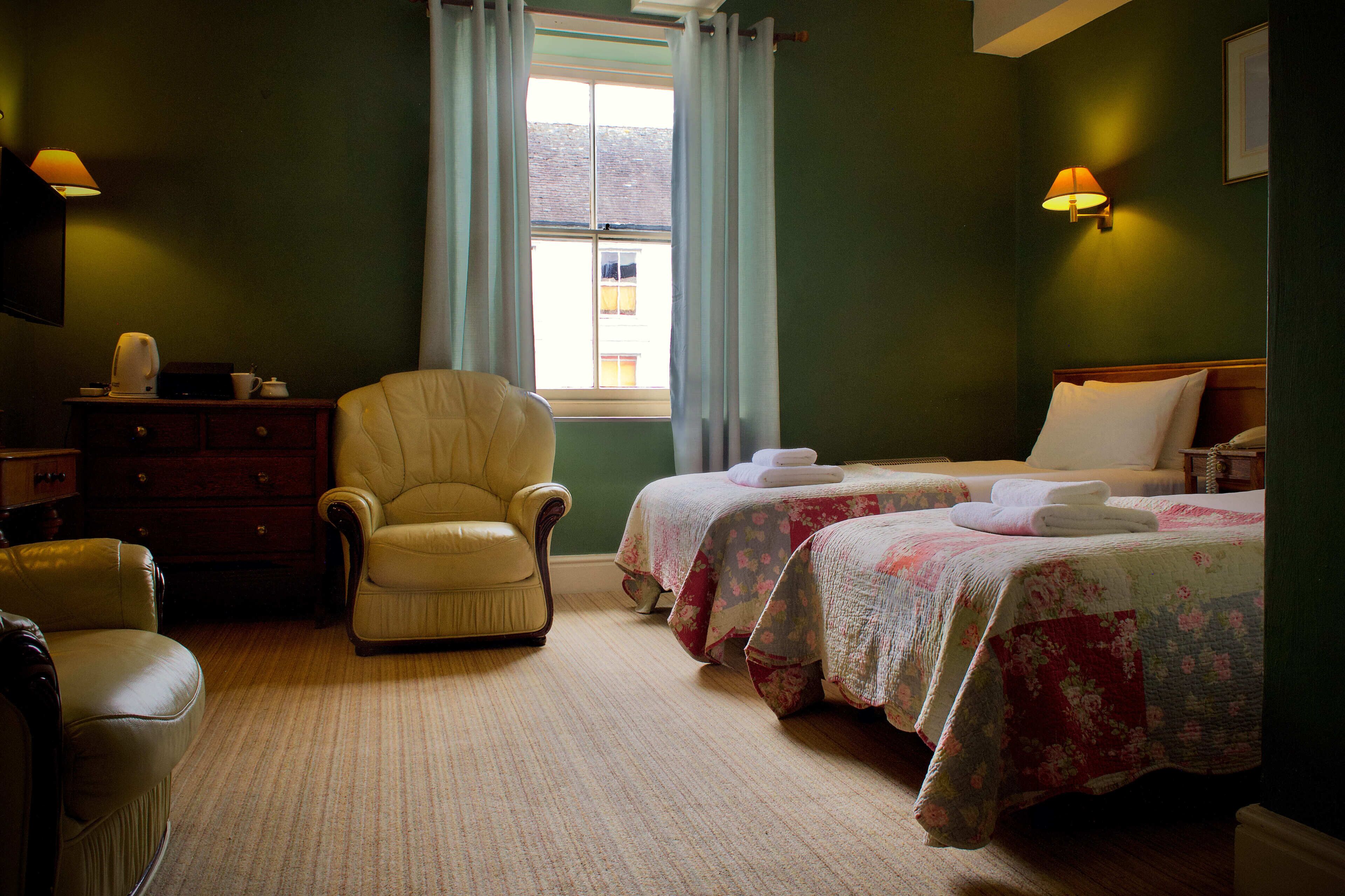 A hotel room with two beds, a chair, a dresser, and a window with curtains.