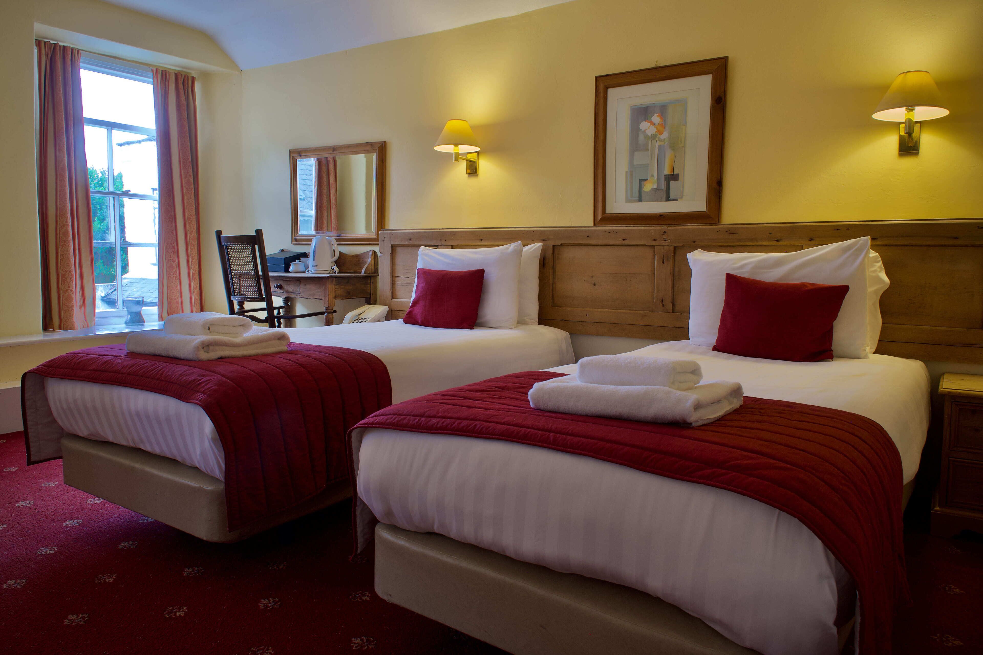 A hotel room with two beds, a desk, a chair, and a window with curtains.