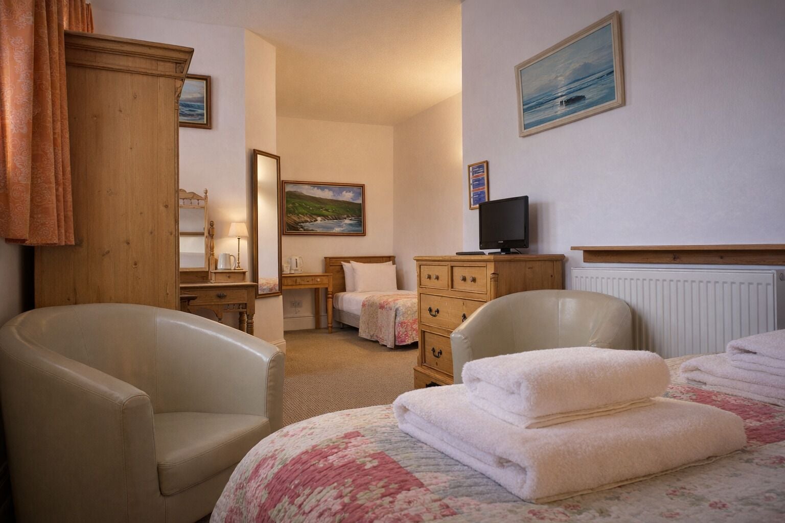 A hotel room with a bed, two armchairs, a wooden dresser, a television, and a painting on the wall.