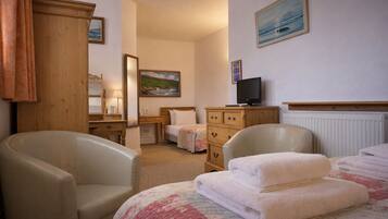 A hotel room with a bed, two armchairs, a wooden dresser, a television, and a painting on the wall.