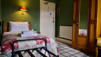 A bedroom with a bed, a nightstand, a wooden wardrobe, a radiator, and a wall-mounted lamp.