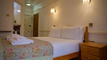 A hotel room with a bed, a nightstand, two wall sconces, a wooden nightstand drawer, and a door leading to another room.