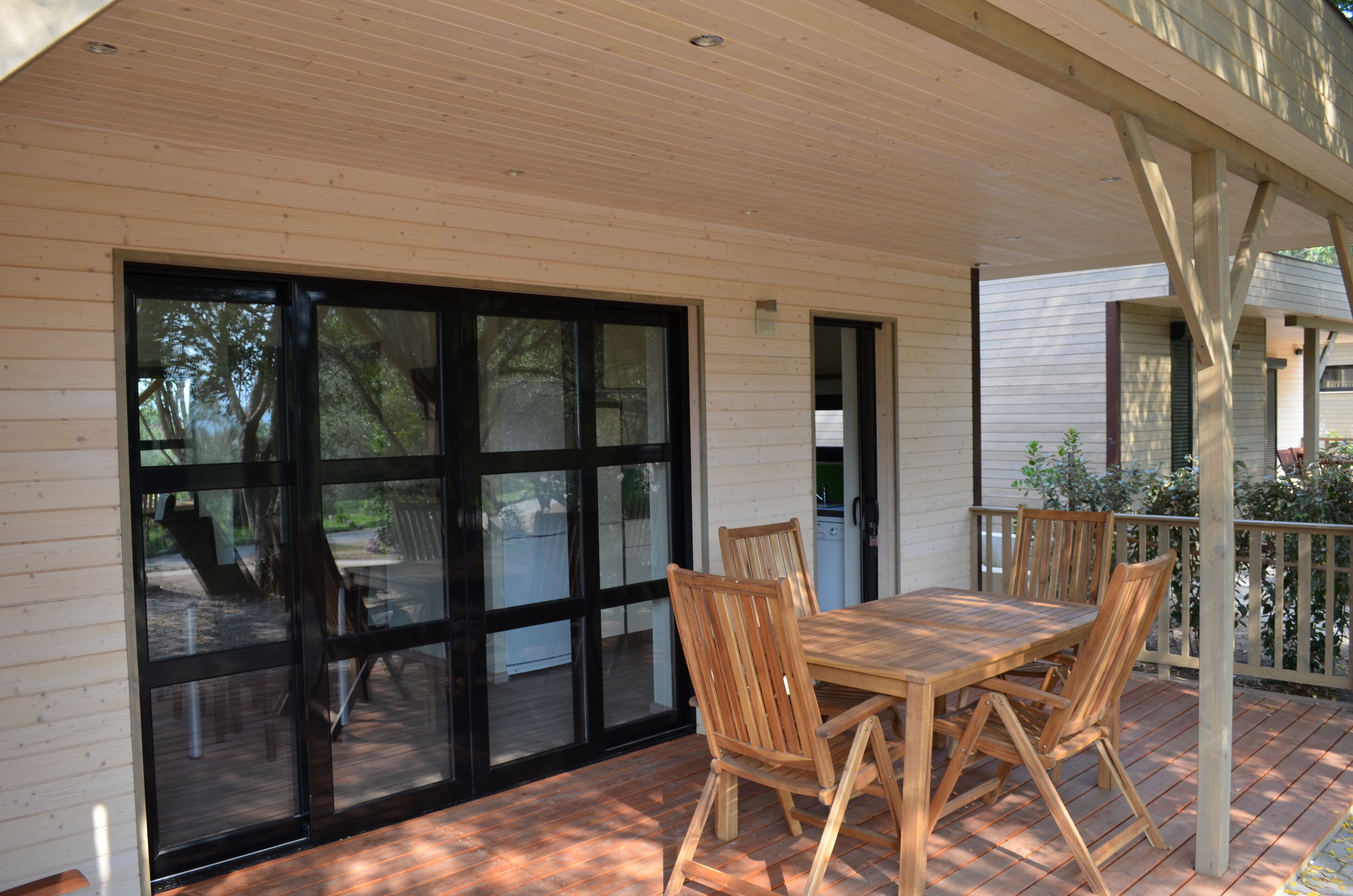 Une terrasse couverte avec une table et des chaises en bois, de grandes portes-fenêtres coulissantes et une vue sur l’extérieur.