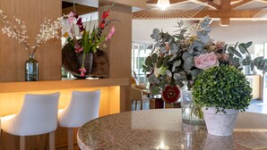Una mesa redonda con cubierta de granito, rodeada de sillas blancas y decorada con arreglos florales en jarrones de vidrio.