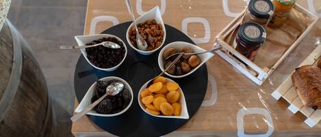 A table with various food items and condiments, including bowls of dried fruits and nuts, a tray with jars, and a piece of bread.