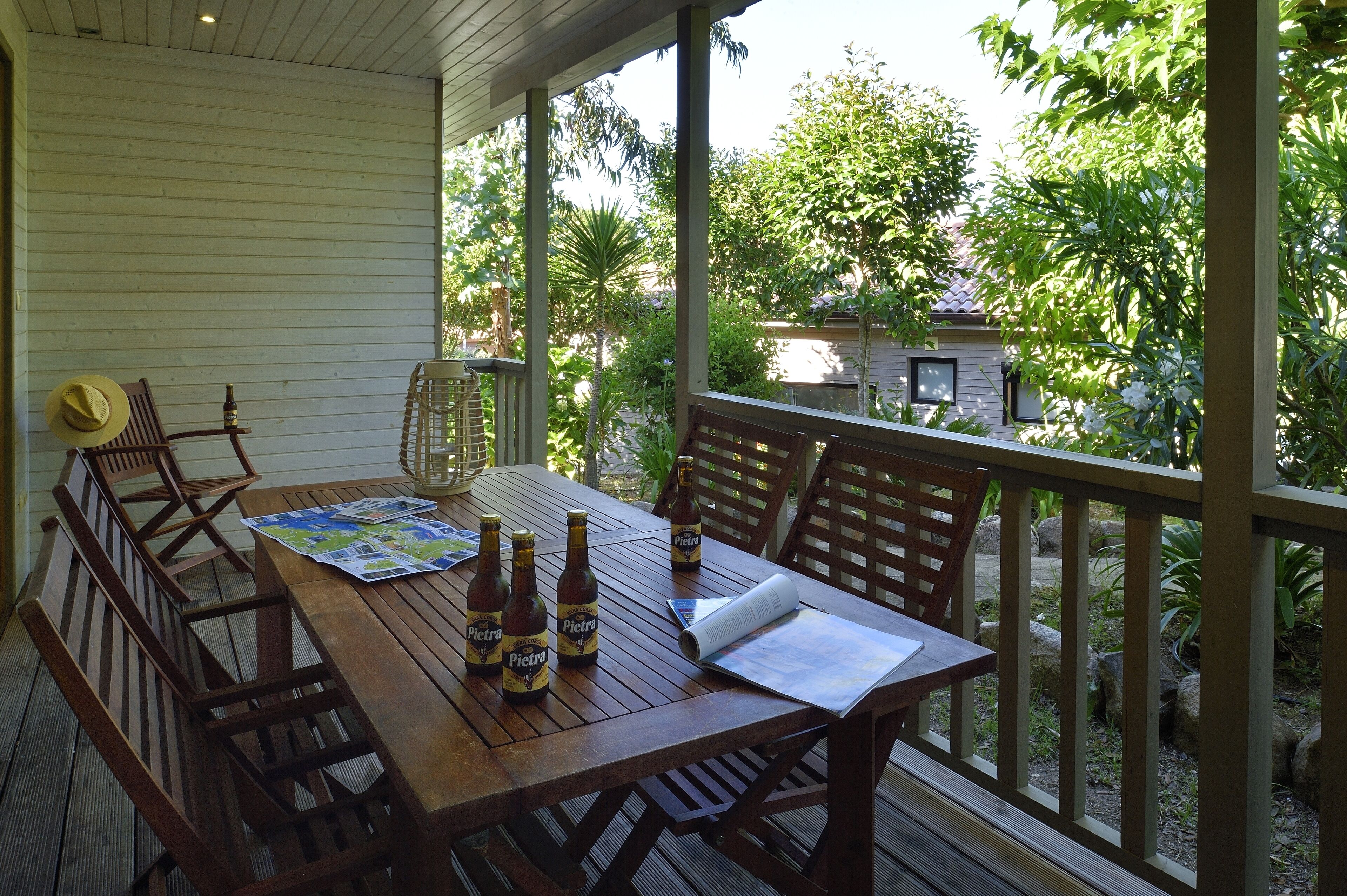 Una terraza de madera con una mesa lista para dos personas, que incluye un mapa y botellas de cerveza.