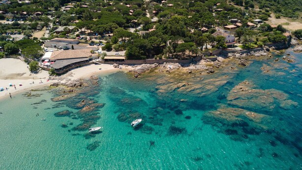 Vista aérea de una zona costera con aguas turquesas cristalinas, costas rocosas y una playa de arena.