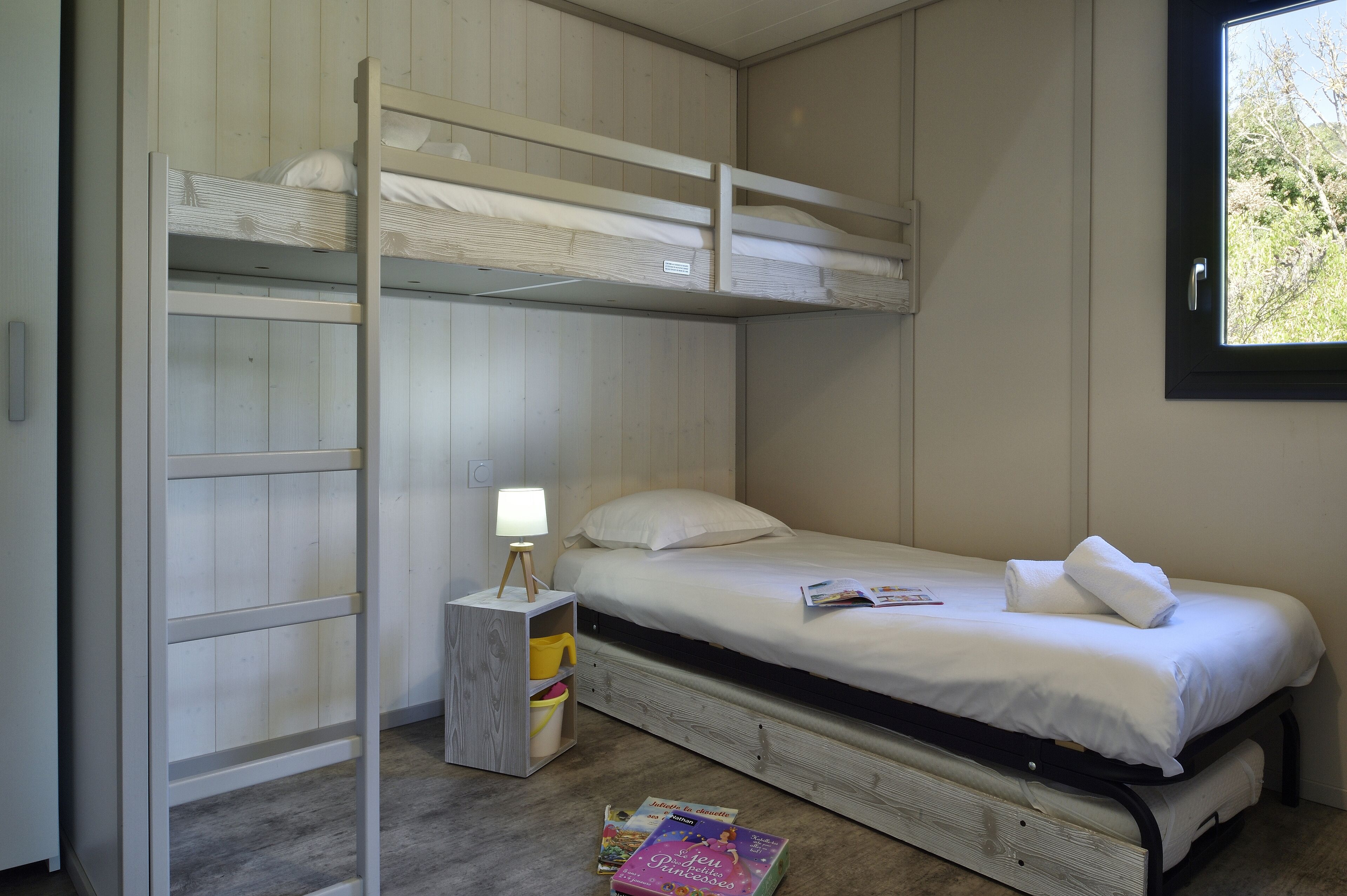 Une chambre avec un lit superposé, une petite table de chevet, une lampe et une fenêtre.