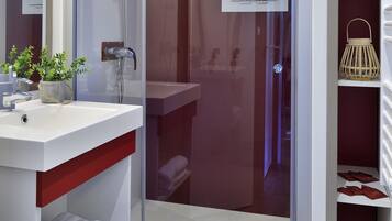 A modern bathroom with a glass-enclosed shower, a white sink with a plant, and a wicker basket with towels.