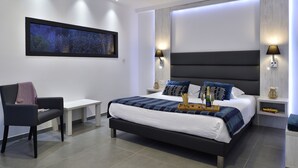 Un dormitorio moderno con una cama grande, mesitas de noche, un banco y un televisor montado en la pared.
