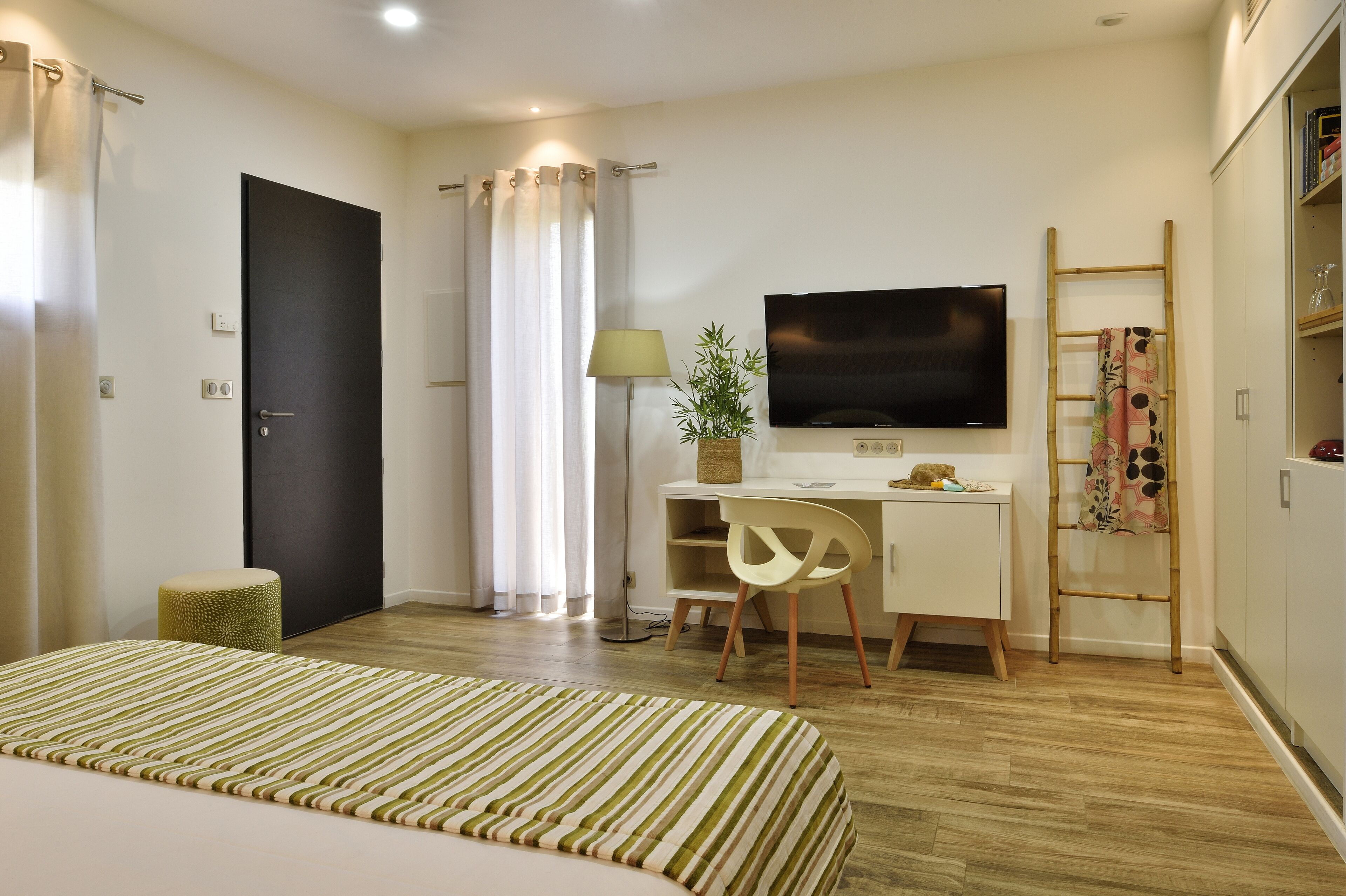 Ein modernes Hotelzimmer mit einem Bett, einem Schreibtisch mit Stuhl, einem Fernseher und einem Kleiderschrank.