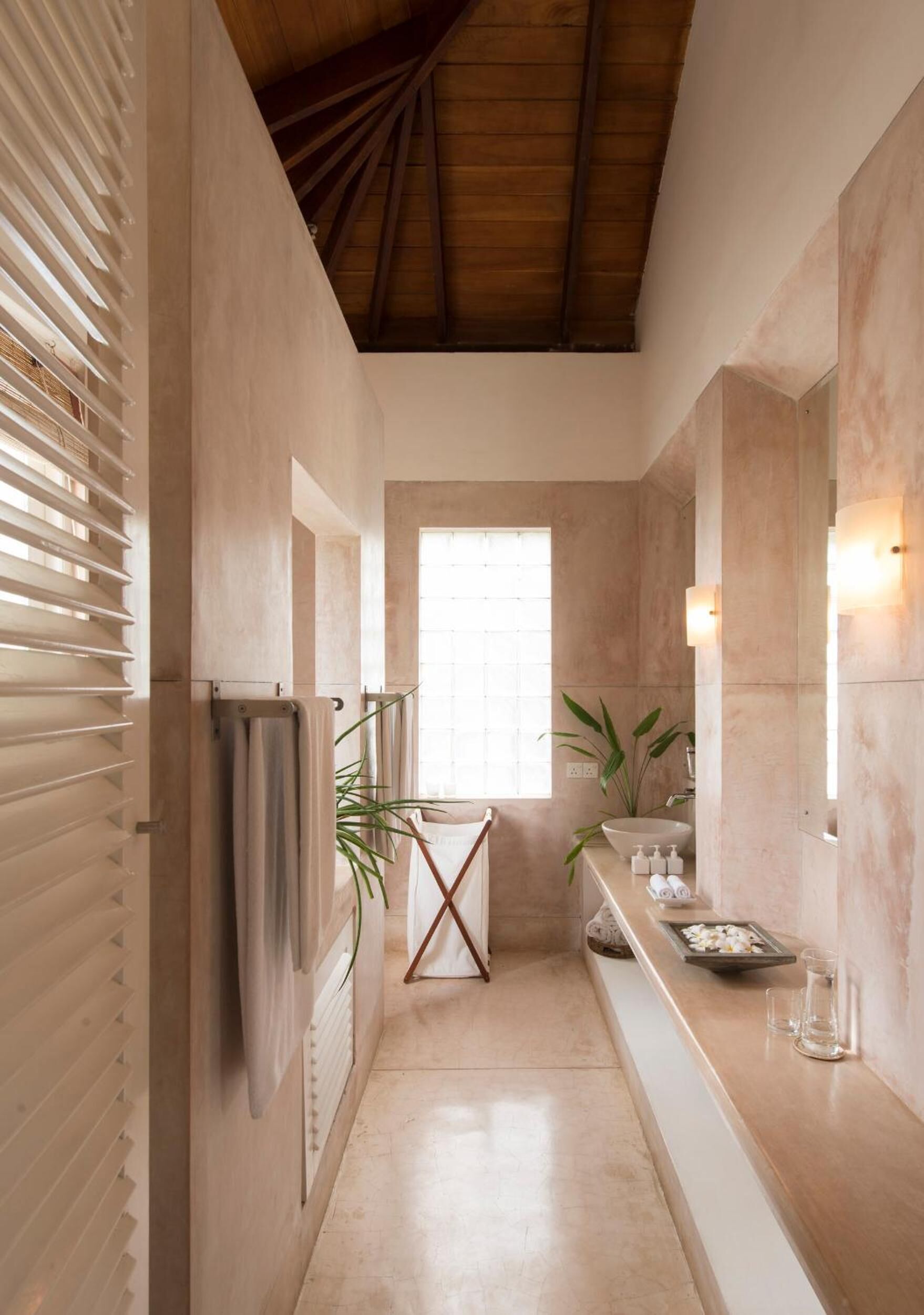 A narrow, well-lit hallway with a wooden ceiling, a large window, and a plant on the right.