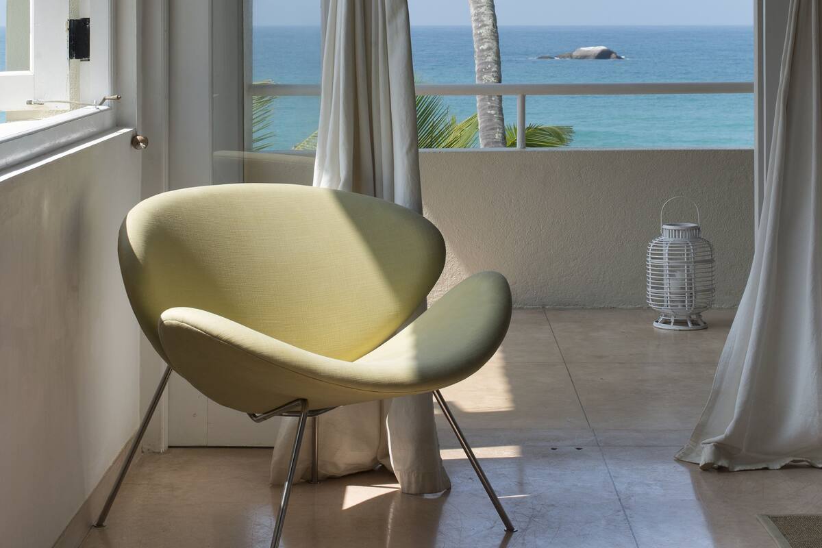 A room with a view of the ocean, a chair, and a white lamp.