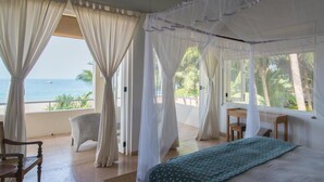 A bedroom with a bed, a chair, a desk, and a view of the ocean. - Sri Villas (Induruwa)