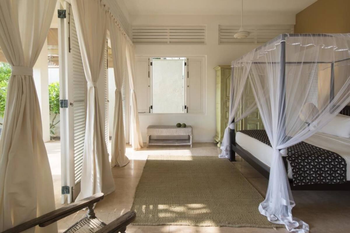 A bedroom with a canopy bed, a bench, and a view of the outdoors.