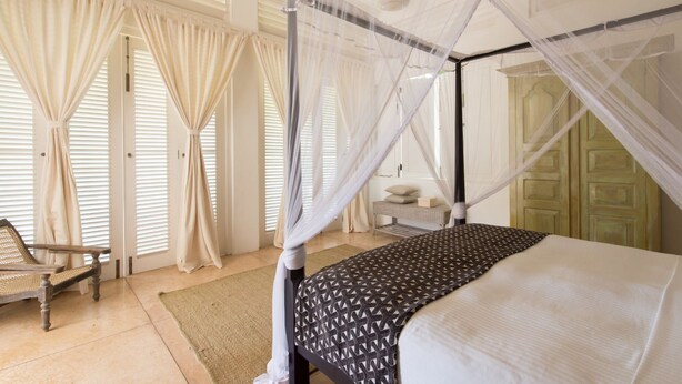 A four-poster bed with a canopy, a wicker chair, and a small bedside table with a lamp. - Sri Villas (Induruwa)