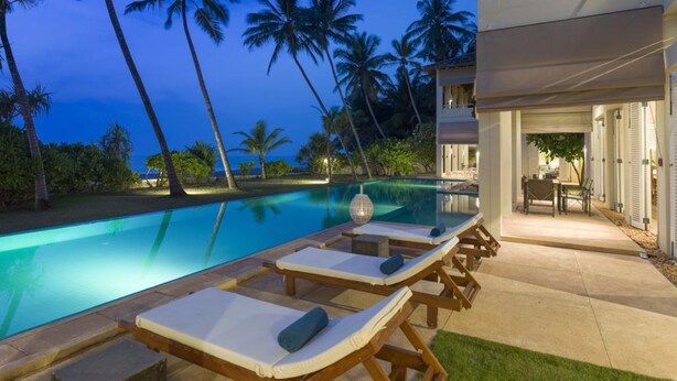 A poolside area with lounge chairs and a view of the ocean at dusk. - Sri Villas (Induruwa)