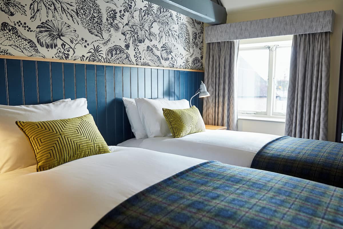A hotel room with two beds, a patterned wall, a window with curtains, and a headboard.