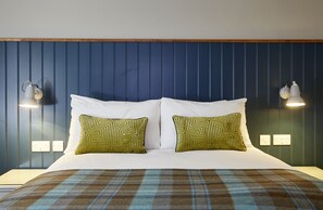 A hotel room with a large bed, two patterned pillows, a plaid bedspread, and wall-mounted lamps. - Pen & Parchment Inn by Greene King Inns (Stratford-upon-Avon)