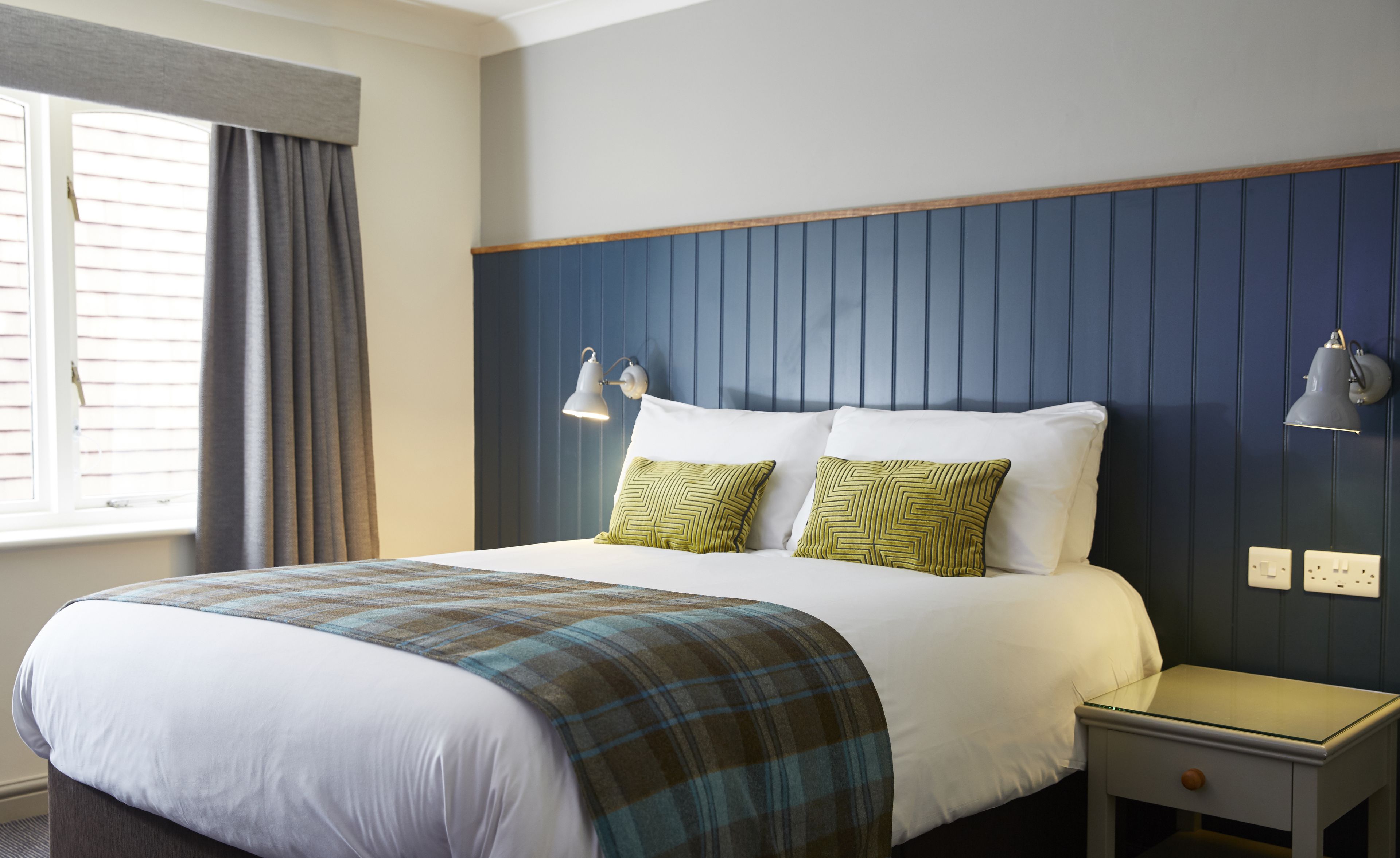 A hotel room with a bed, two bedside lamps, a nightstand, and a window with curtains.