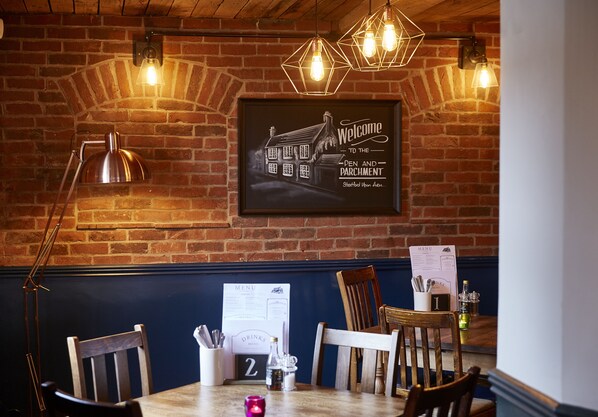 L’intérieur d’un restaurant avec des murs en briques, des chaises en bois, une table avec un menu et des luminaires suspendus.