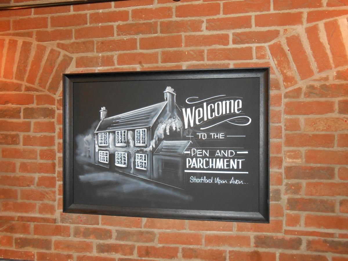 A framed welcome sign with a house illustration and text for 'Pen and Parchment' in Stratford-upon-Avon.