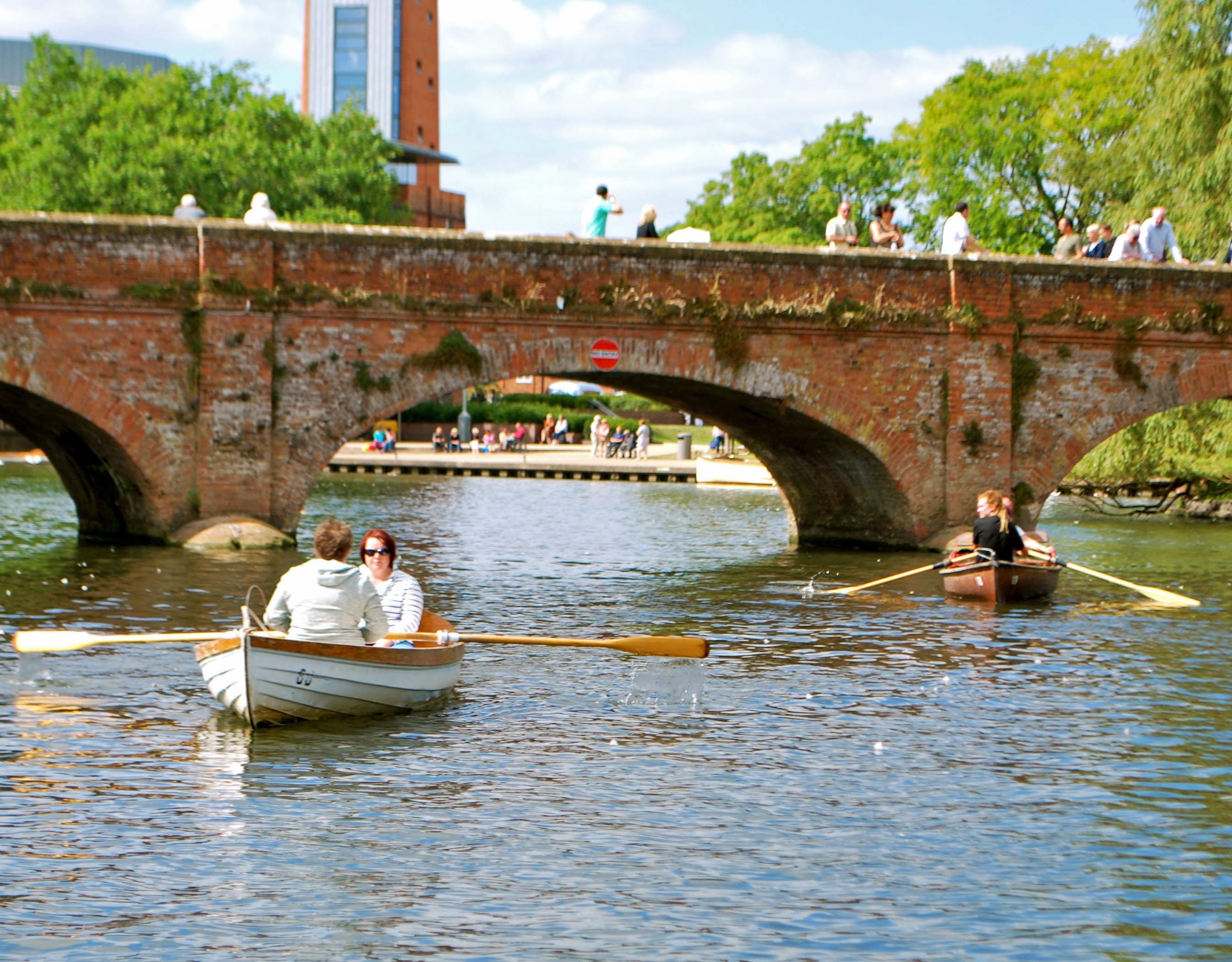A river scene with a bridge, boats, and people.