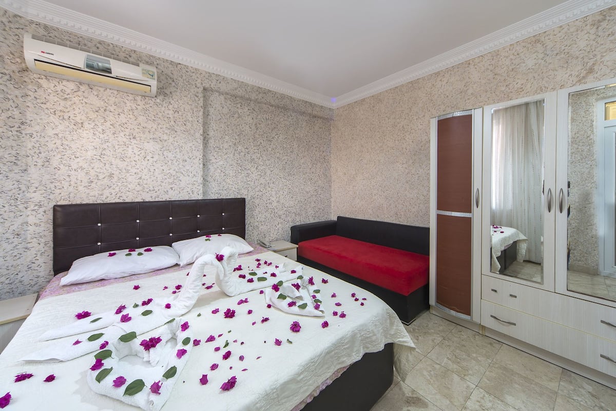 A hotel room with a bed, a red sofa, a wardrobe, and an air conditioning unit.