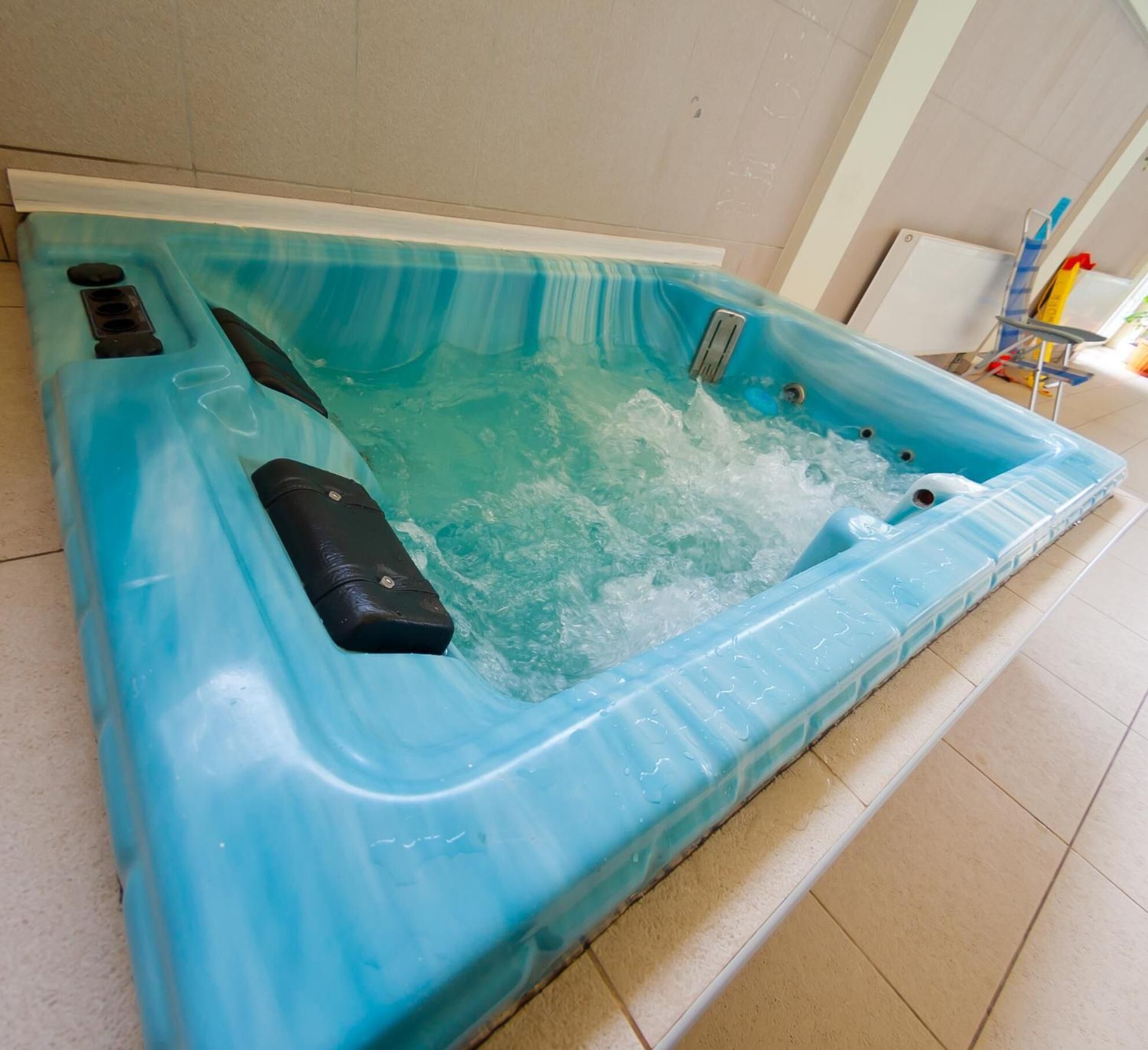 A rectangular hot tub with a blue interior, a control panel on the left, and a drain in the center.