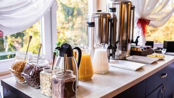 Mostrador de l'esmorzar amb diferents aliments i begudes, incloent pots de granola, xocolata i una garafa de suc d'aranja, amb una cafetera i una testosseta de llet al fons.