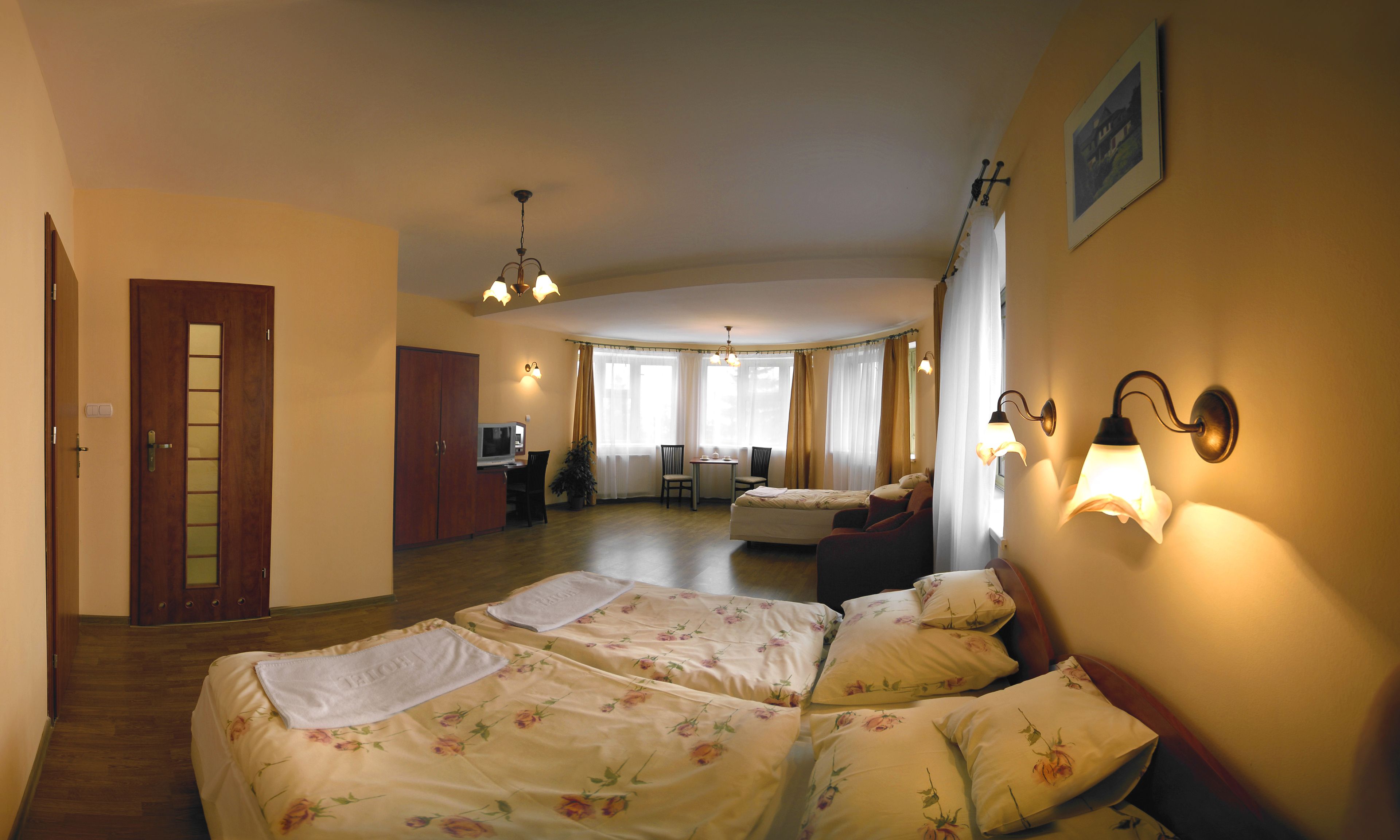 Habitación de hotel con dos camas, un escritorio y una silla. Se ve una puerta y una ventana con cortinas.