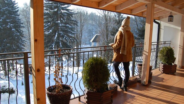 A wooden balcony with metal railings, potted plants, and a view of a snowy forest. - Dom Wczasowy Beskidy (Wisla)