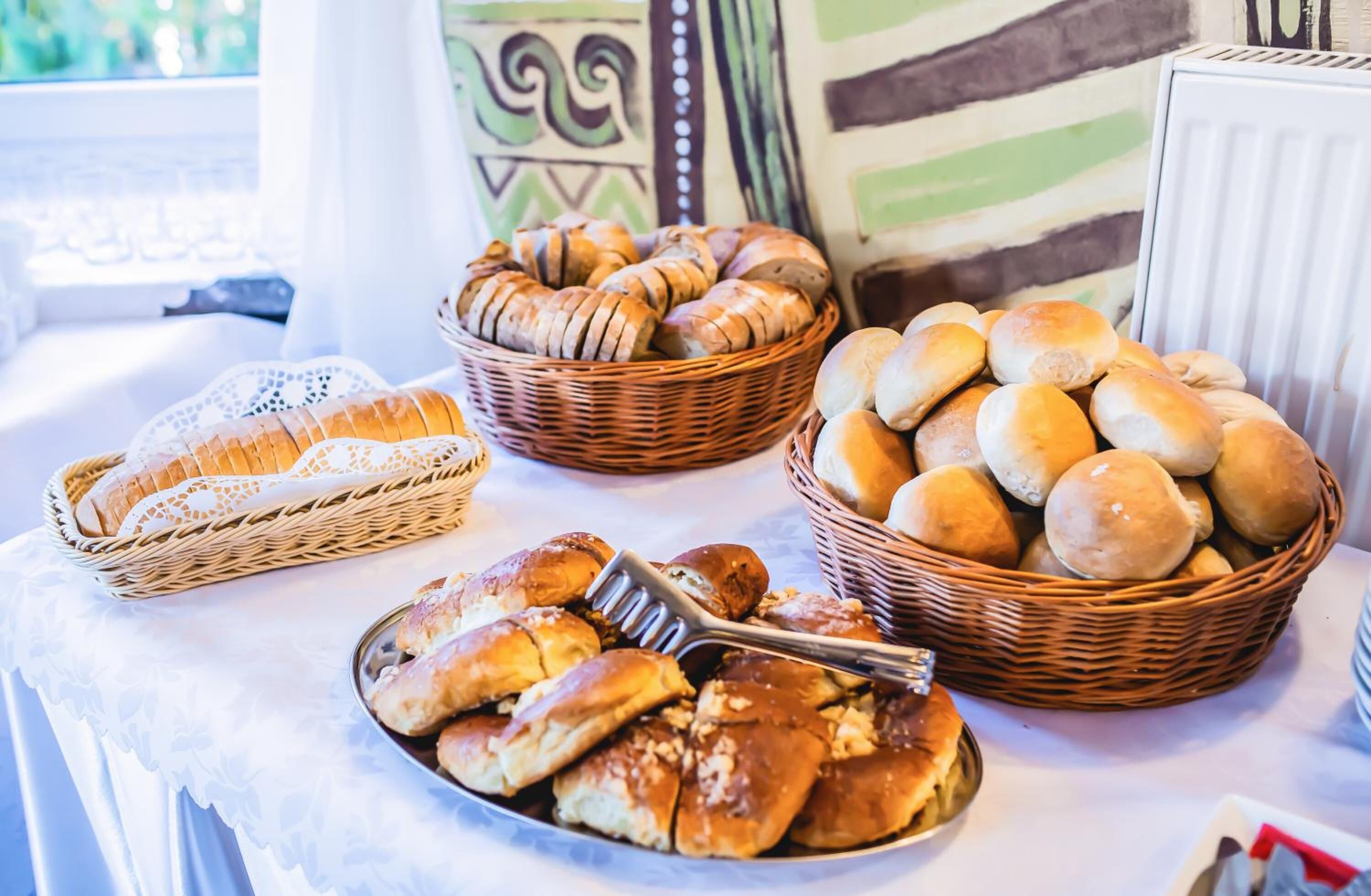 Ein Tisch mit verschiedenen Brotsorten und Gebäck, darunter Laibe, Brötchen und Hörnchen, die in Körben und auf einem Teller angerichtet sind.