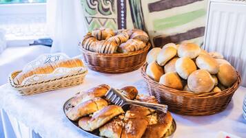 Ein Tisch mit verschiedenen Brotsorten und Gebäck, darunter Laibe, Brötchen und Hörnchen, die in Körben und auf einem Teller angerichtet sind.